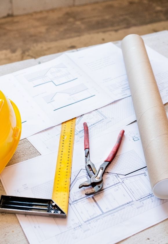 Plans architecturaux avec casque jaune, mètre ruban, pince et rouleau de papier sur table en bois