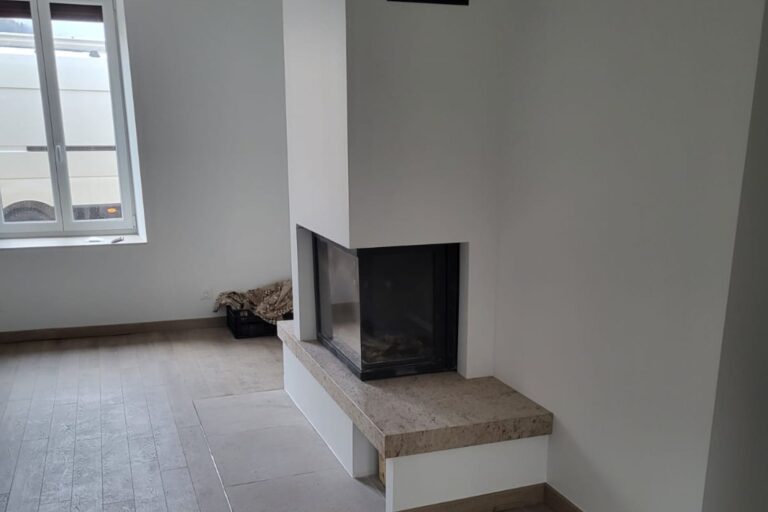 Intérieur moderne avec cheminée centrale en pierre et foyer noir intégré, murs blancs et grandes fenêtres